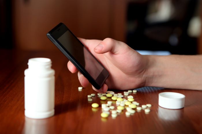 Hand holding phone over a table of pills
