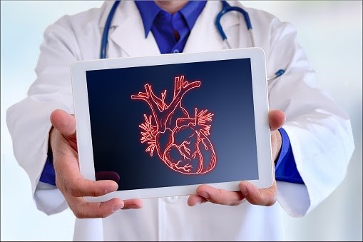 Doctor in a white coat holding out a mobile tablet with an image of an anatomical heart on it.